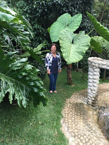 Dr. Orozco-Cardenas in the rainforest standing next to leaves almost as long as she is tall and as wider than she.